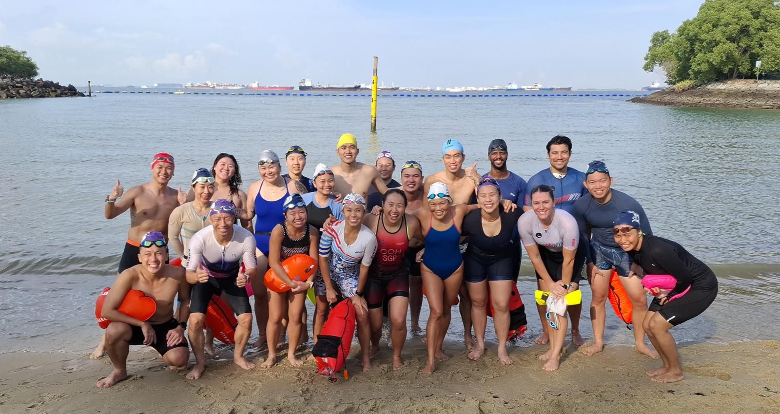 About twenty smiling swimmers in caps and goggles at Tanjong Beach, Sentosa