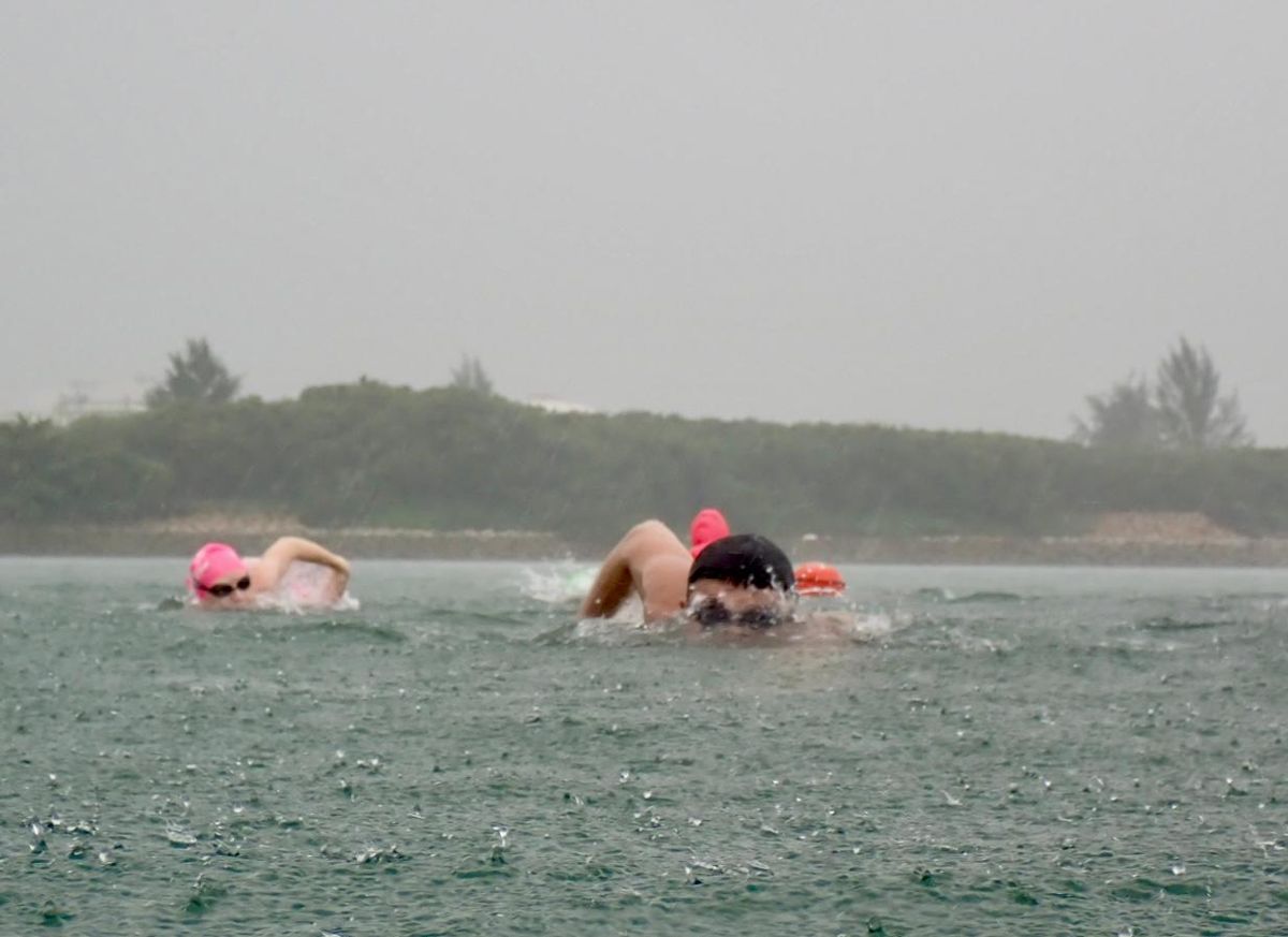 Open water swimmers in pink and black caps during a rainy swim